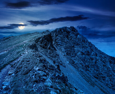 mountain scenery in summer at night. gorgeous mountainous landscape. background with rocky cliffs and grassy hillsides under a cloudy sky. full moon over ridge of mysterious mountains