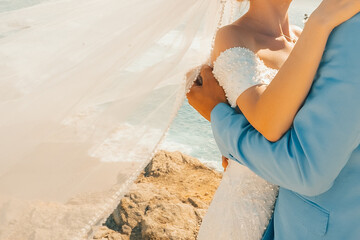 Couple embraces by ocean during wedding ceremony at sunset near shore.  couple stands close,  wedding ceremony by the ocean. sun sets in background, creating warm atmosphere as they celebrate love. © SValeriia