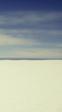 Snow covers the ground in a vast area. Mountains rise in the background under a blue sky with some clouds. It is daytime and the scene suggests a cold environment.