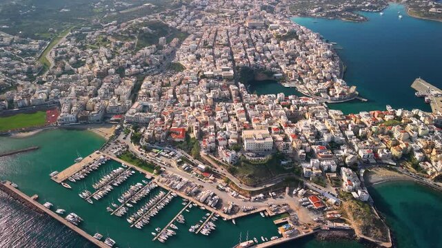 Aerial view of Agios Nikolaos city and Lake Voulismeni in Crete, Greece. Drone flight over yacht marina, circular lake and scenic coastline of Mirabello Bay at sunny morning. Urban landscape 4k.
