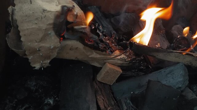 Macro closeup kindling flames over charcoal in backyard grill, paper and small wood catching fire, soft orange glow, smouldering embers, gentle smoke rising, close textured detail and lowlight