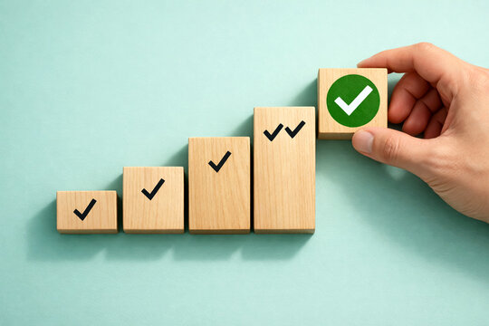 Businessman hand adding a final wooden block with a green check mark to a rising staircase to demonstrate the successful accomplishment of key corporate performance. Business growth success achievemen