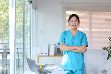 Smiling asian female doctor or nurse in a blue uniform standing in a clinic or hospital office,...