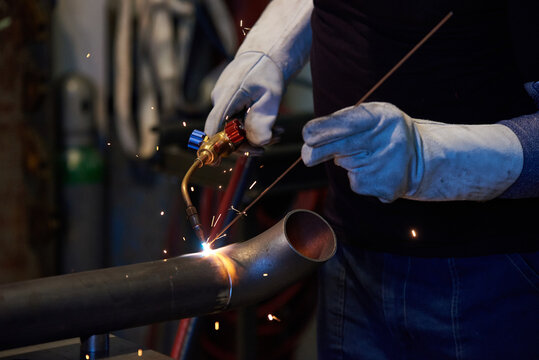 Manual worker welding metal pipe with gas torch and sparks in industrial factory, Katowice, Silesian, Poland, Europe.