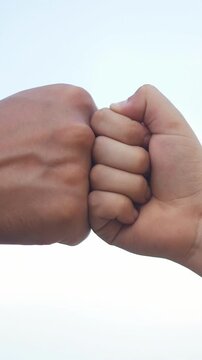Two hands are bumping fists in a gesture of camaraderie. One hand is larger, showing the diversity of hands in this moment of connection.