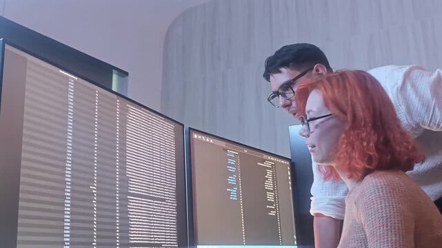 Programmers working at night analyzing code on monitors in a modern office. Software developers collaborating on debugging cybersecurity and data programming projects. Ai coding Software technician.