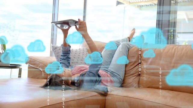 Teen female reclining on sofa holding tablet, tapping and creating cloud overlays for cloud sync