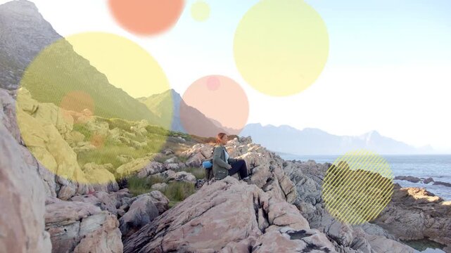 Woman adjusting blue bag, gazing sea, starting bokeh circles sweeping over her and rocks for design