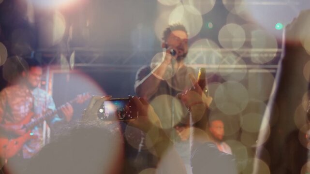Male vocalist singing in concert, phone clip spurring crowd filming to capture music with bokeh