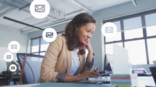 Female office worker typing at laptop in office, managing incoming email icons appearing from left