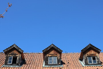 Obraz premium Three Dormer Windows on an Old Tiled Roof Against a Blue Sky