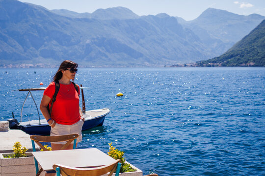 Woman solo traveler exploring Kotor city in Montenegro. Female tourist looking at sea bay and surrounding mountains. Active summer vacation