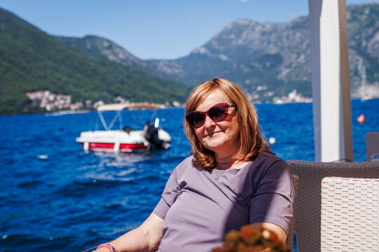 Happy mature woman sitting in outdoor cafe at sea bay in Kotor city in Montenegro. Summer holiday