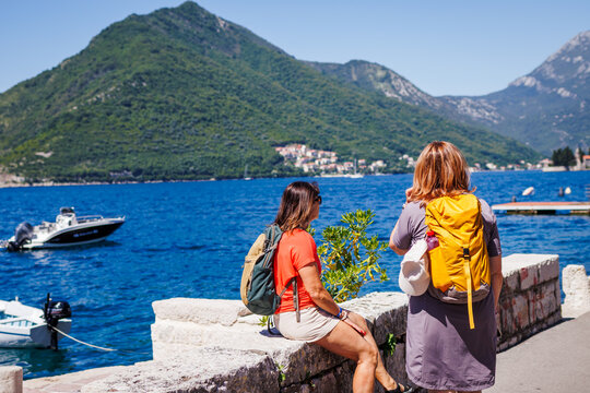 Two women travelers enjoying view at bay of sea in Kotor, Montenegro. Active vacation at summer. Female tourists with backpack