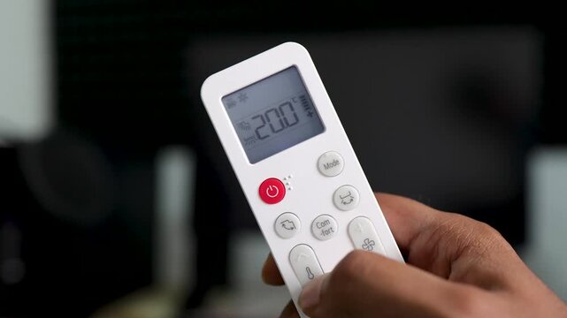 Hand Holding Air Conditioner Remote Control Adjusting Temperature to 16&deg;C, Cooling Down Room with AC for Indoor Climate Control.