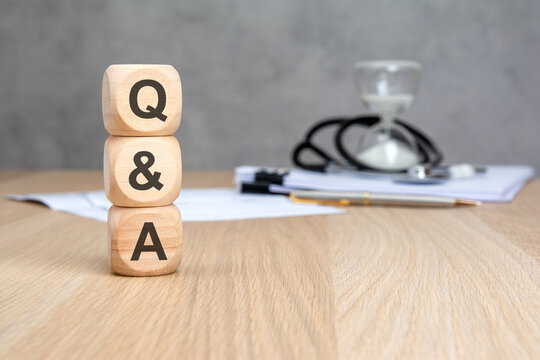 Q and A text on wooden blocks with blurred stethoscope and hourglass. Medical health questions, answers, consultation and time management concept.