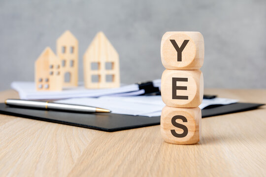 Stacked wooden blocks with YES text blurred house models and clipboard.