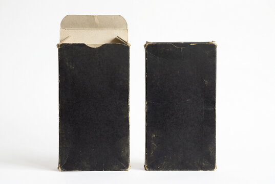 Two worn black cardboard boxes photographed on a clean white background. One box is open with visible beige cardboard flaps, while the other is closed.
