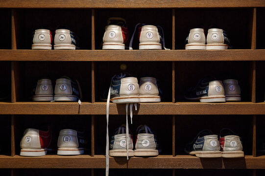 Vintage bowling rental shoes organized in wooden cubby shelves grid pattern indoor ambient lighting sports retro footwear rental
