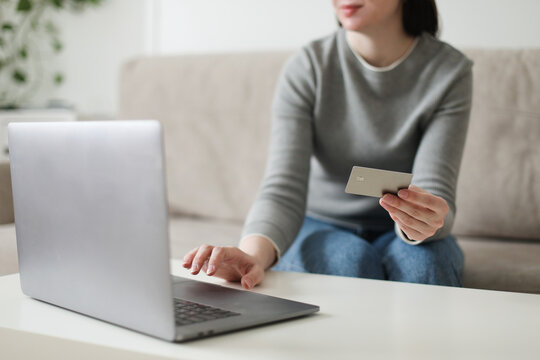 Young woman holding credit card and using laptop at home. Paying online, home shopping, internet banking, electronic store concept