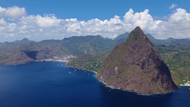 Stunning aerial drone footage captures majestic Piton mountain rising dramatically from deep blue Caribbean waters in Saint Lucia, with lush green tropical forests, coastal town.