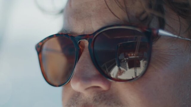 Close up portrait of the young man wearing sunglasses with reflection of the sailing boat. Person sailing, boat reflects in his sunglasses