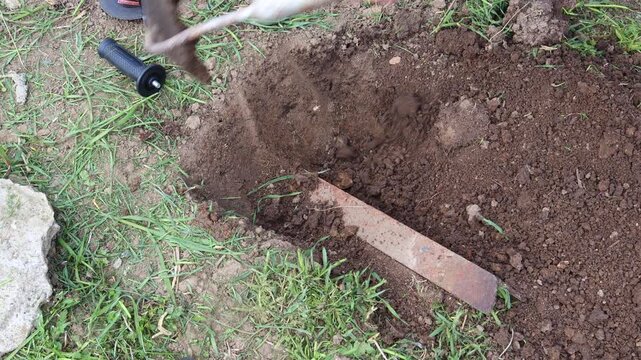 Person digging a ditch in the garden with a grub hoe for planting, ground preparation for agriculture or landscaping with a mattock, moving earth and soil to make a trench