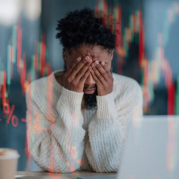 Man distressed covering face at desk with market graph overlay