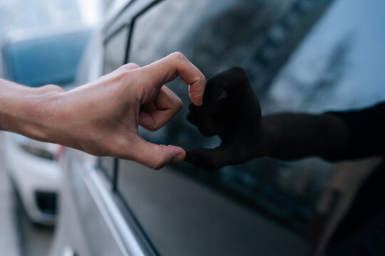 Person hand forms half heart against car window. Dark reflection completes shape, symbolizing self love or solitude. Cool blue tones and blurred background create thoughtful, lonely mood.