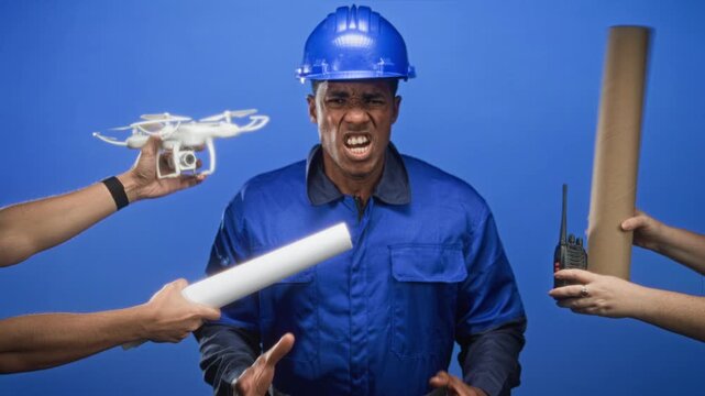 Man construction worker grimacing as hands present drone, walkie and rolled plans toward him in studio; teamwork frustration.