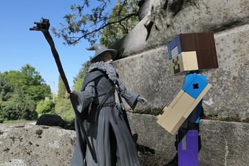 Obraz premium Minecraft figure of main character Steve greets action figure of wizard Gandalf from novel Hobit and Lord Of The Rings by J.R.R.Tolkien under ancient stone pedestal of lion statue, spring sunshine. 