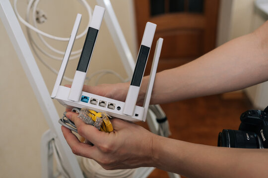Close-up of hands holding modern white wireless router. Person connecting ethernet patch cords to ports for internet setup. Concept of home network, connectivity, data, technology.