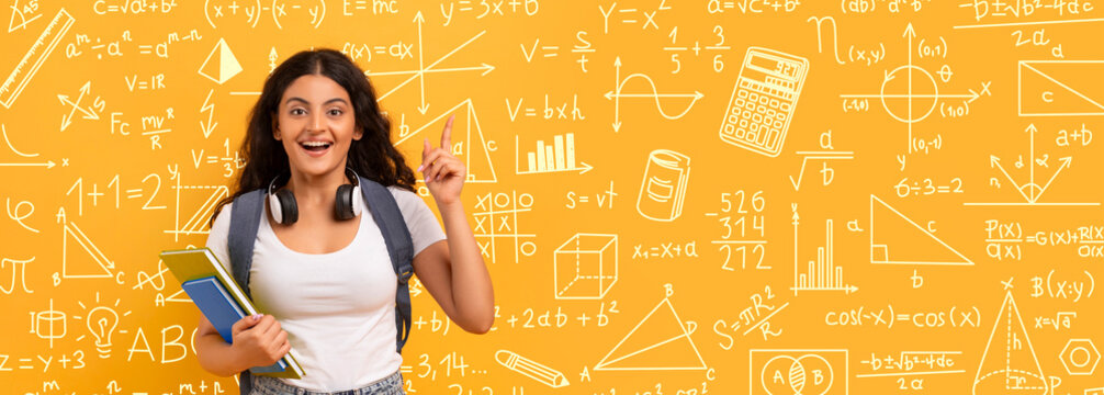 A student stands against a bright yellow wall filled with math symbols and equations. She holds notebooks and gestures with one hand, showing excitement about learning or discovering something new.