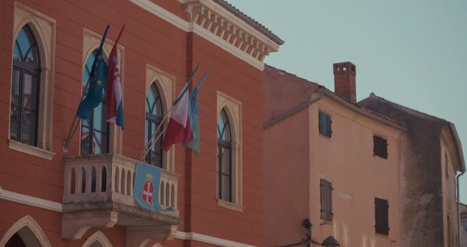 A municipal building facade with arched windows and a balcony displaying multiple flags is shown on Square Tomaso Bembo.