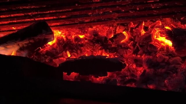 Glowing coals and dancing flames close-up outdoors. Burning coals with flickering flames, fiery texture close-up