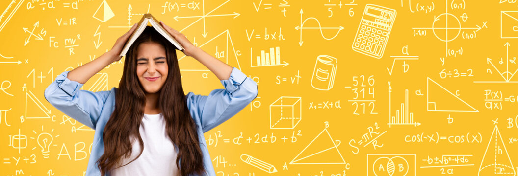 A student struggles with math while holding a book on her head. She is in a room filled with math symbols and formulas written on a yellow wall. The time of day and exact location are unclear.