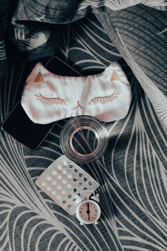 Insomnia medication, water, a smartphone, and a mask on the bed top and vertical view
