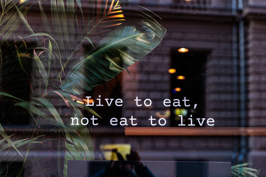 Live to Eat Sign On Cafe Window With Plants And Street Reflection