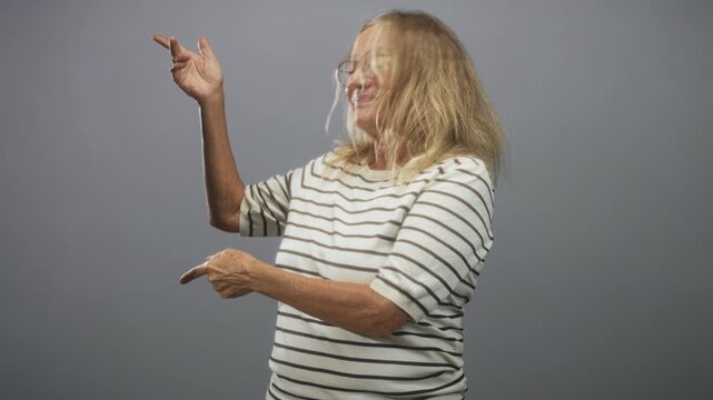 Woman pointing finger with visible hand in a grey studio, smiling and gesturing toward the side; joyful playful energy.