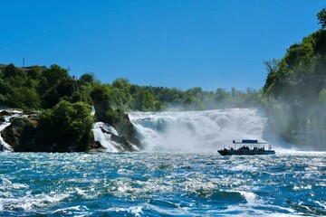 Tour boat approaching Rhine Falls in Switzerland with dramatic cascading water and blue summer sky © svenja