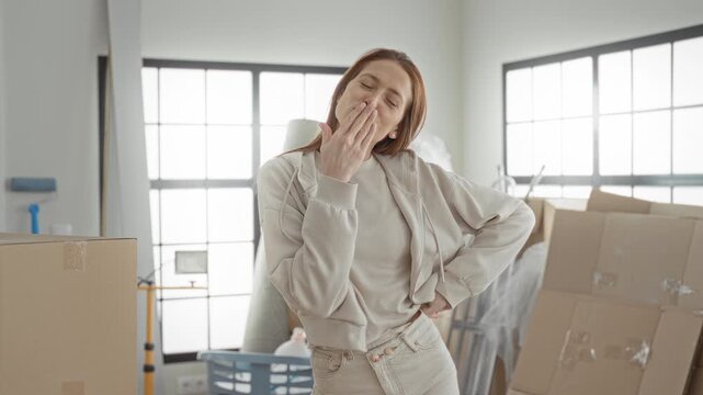 Woman smiling and blowing a kiss, hand on hip surrounded by cardboard boxes in apartment; moving day joy.