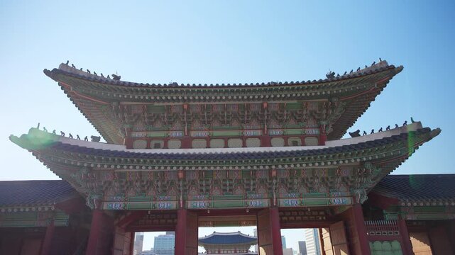 Majestic Gyeongbokgung Palace gate showcases intricate traditional Korean architecture with ornate wooden brackets, colorful dancheong paintwork, and curved tiled roofs against clear blue sky in.
