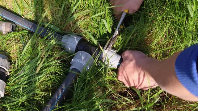 Plumber tightening a plastic pipe fitting on a water supply line in the garden with an adjustable wrench during an emergency repair of the irrigation system