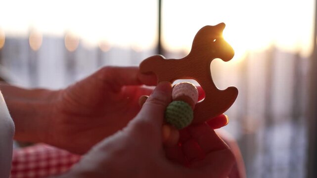 Mother holding eco-friendly wooden horse teether toy for her baby, offering a safe and natural teething accessory for infant gums and development during golden hour sunset