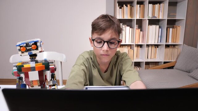 Young boy with glasses studies at a desk, focused on a laptop while a colorful toy robot sits nearby amid books, illustrating modern stem learning and ai curiosity
