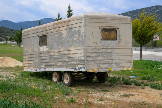 Old abandoned metal trailer parked in a rural field with mountains in the background