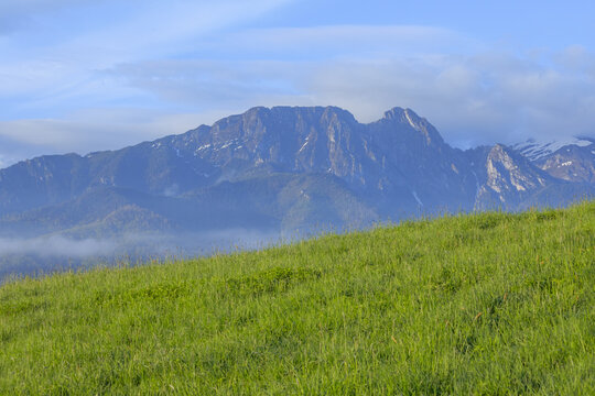 Massive limestone formation of Mount Giewont in Tatra Mountains near Zakopane, Poland. Alpine landscape with green meadow in foreground, clouds and morning mist over Western Tatras, majestic peak.