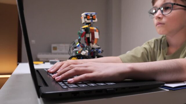 Young boy learning stem concepts and robotics, programming control for his colorful educational robot using a laptop, focusing on innovation and technology