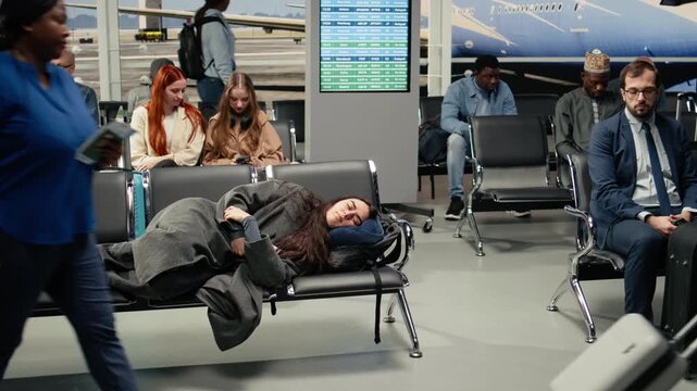 Tired woman in airport lounge sleeping on metal bench during long airplane layover. Jet lagged traveler resting on seats, napping on neck pillow while waiting for delayed plane, camera A