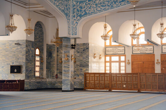 Interior of mosque prayer hall with arches chandeliers columns and mihrab area with carpet rows. Islamic architecture and worship space